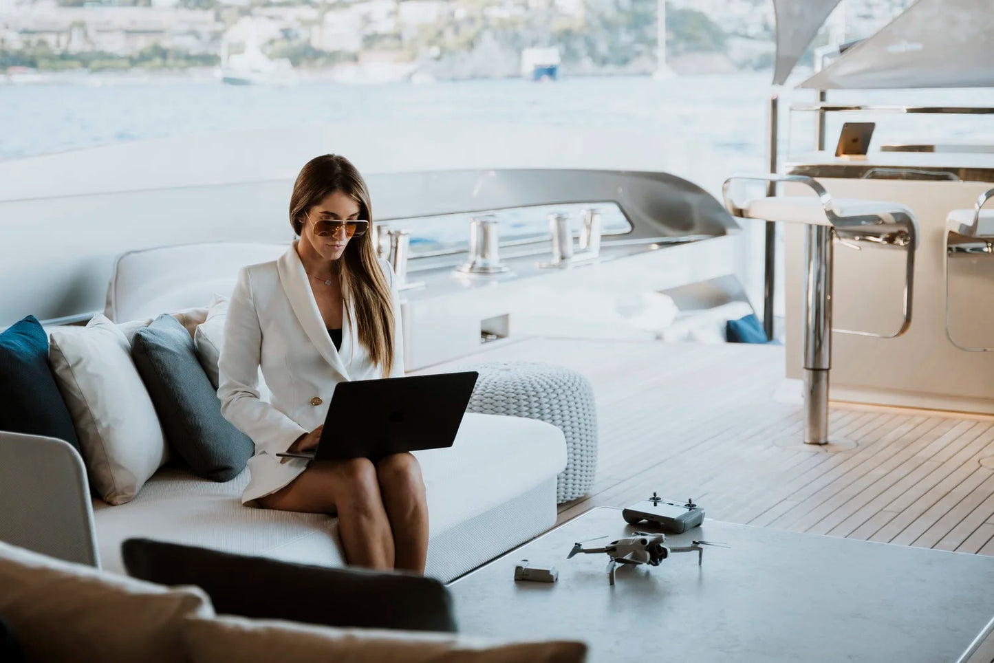 Woman using a laptop on a yacht with a drone on the table.